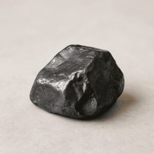 Dunkelgrauer Hämatit-Rohstein mit metallischem Glanz auf hellem Hintergrund – Symbol für Erdung, innere Stabilität und Schutz