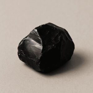 Tiefschwarzer Obsidian-Rohstein auf hellem Untergrund – steht für energetischen Schutz, Schattenarbeit und geistige Klärung